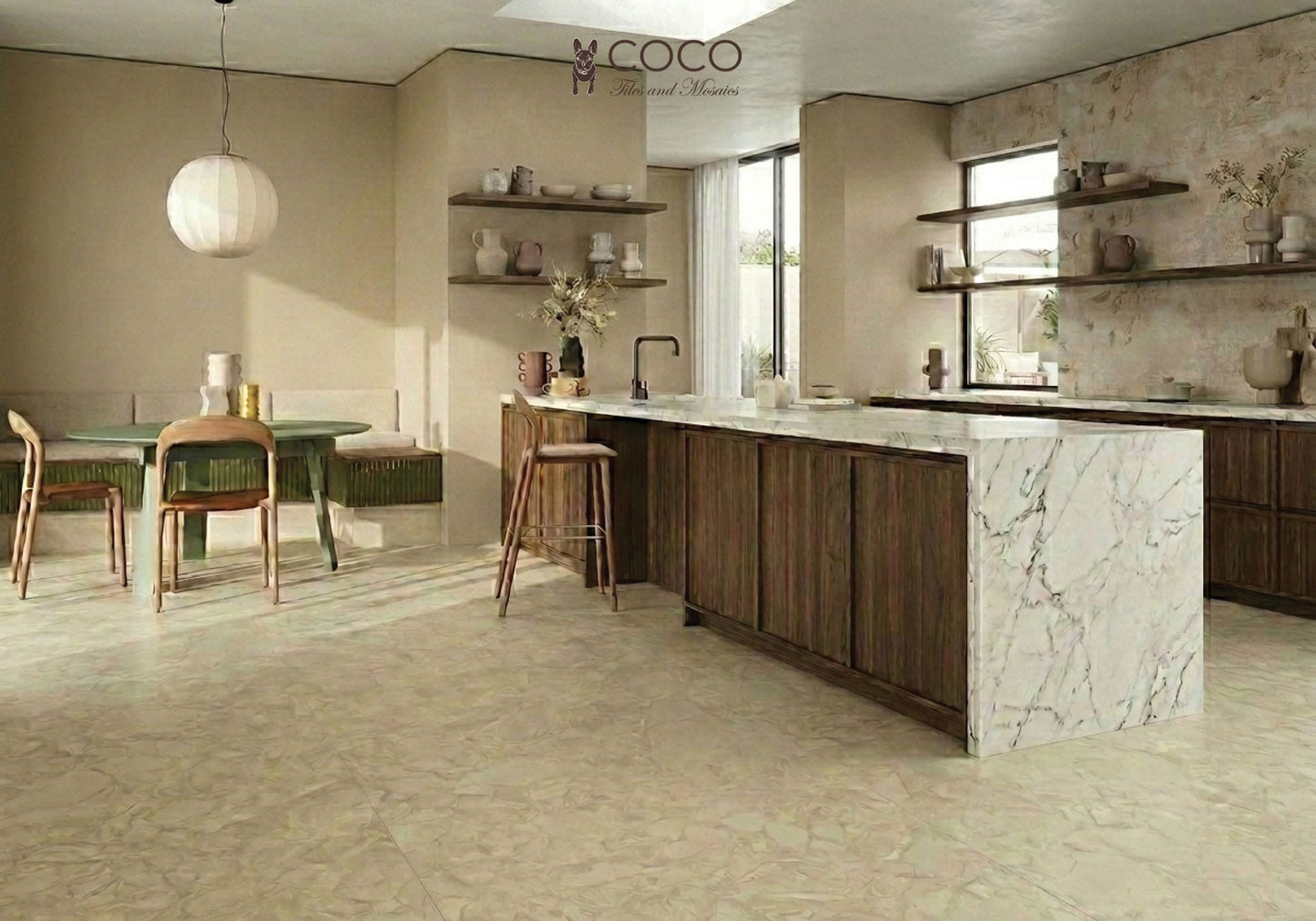 A warm, organic-modern kitchen featuring the Trattoria tile look. The floor is laid with Fragmenta Series Cappuccino 600x600mm creamy beige terrazzo-look tiles. The kitchen wall behind open timber shelving features Babylon Series Villa B 500x1200mm ceramic tiles, displaying a subtle botanical relief pattern with an aged plaster effect. The space includes a marble waterfall island, dark walnut cabinetry, a round green dining table, and a paper lantern pendant light.